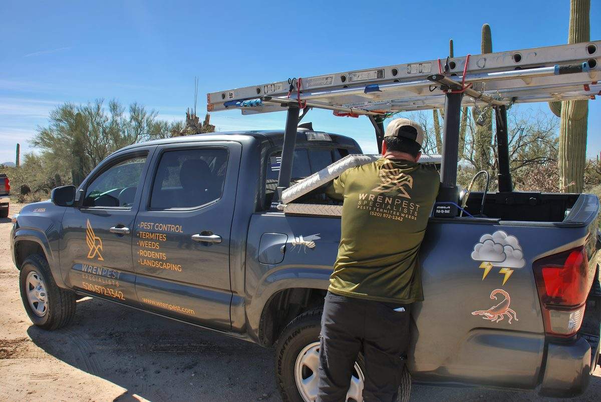 Wren Pest technician gearing up with scorpion treatment equipment from branded service truck in Tucson